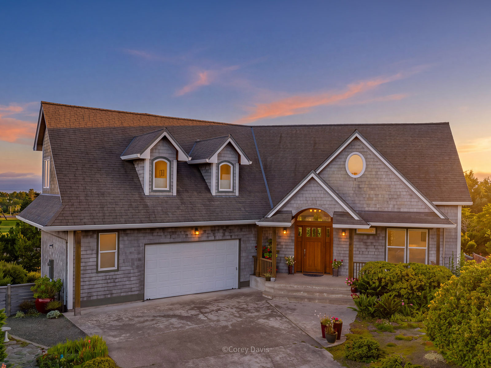 A shingled coastal house at dusk, its windows lit.